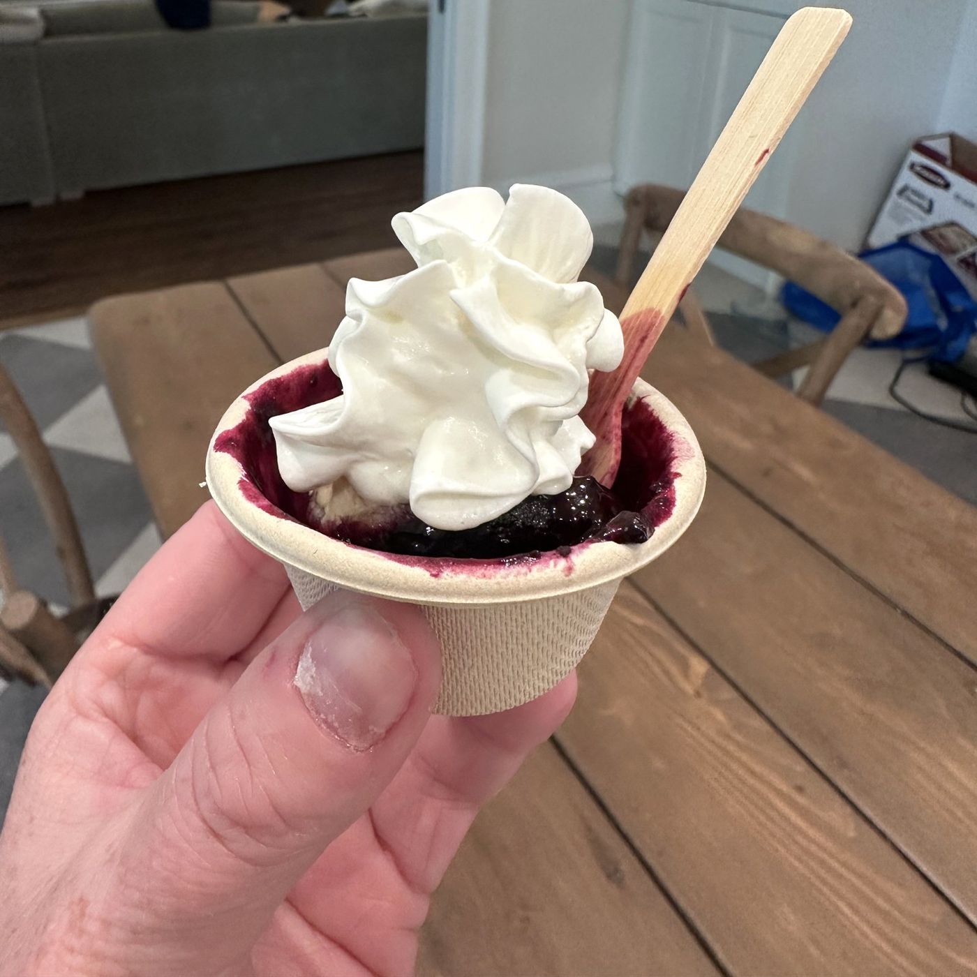 A small paper cup of blueberry grunt topped with whipped cream and a wooden spoon
