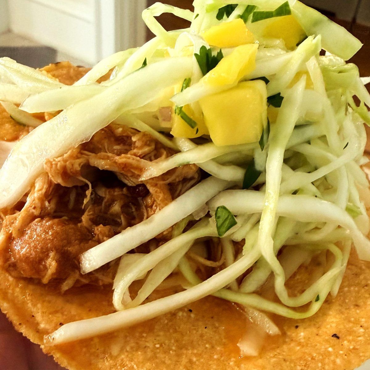 Chicken tinga tostada topped with cabbage slaw and mango