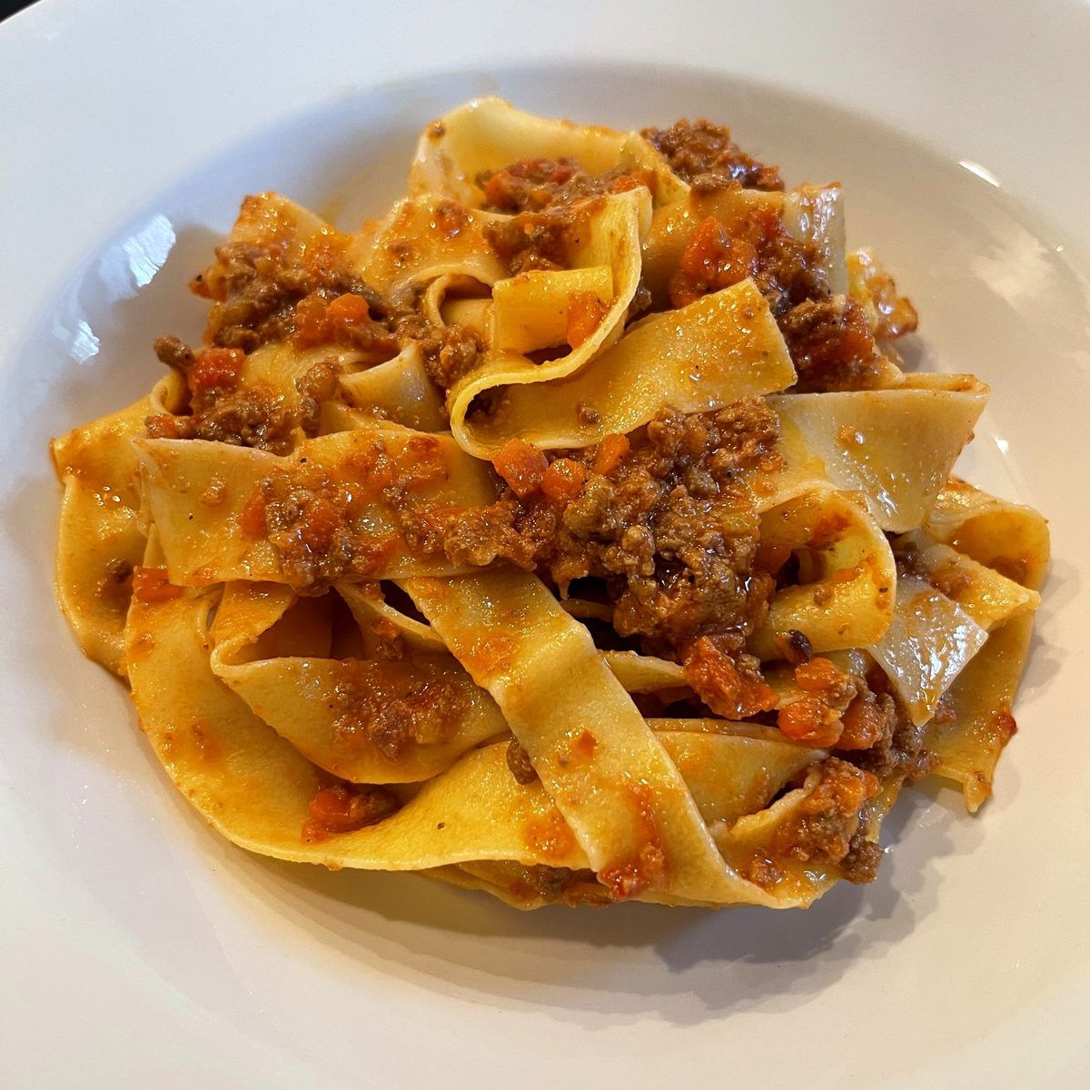 Pappardelle tossed in a rich bolognese in a white bowl