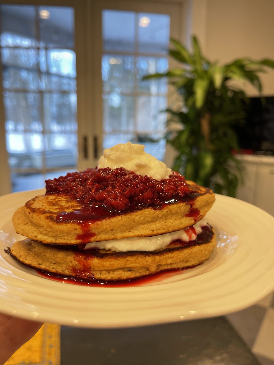 A stack of oatmeal pancakes layered with cottage cheese and topped with berry compote