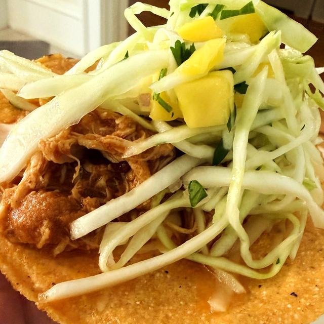 Chicken tinga tostada topped with cabbage slaw and mango