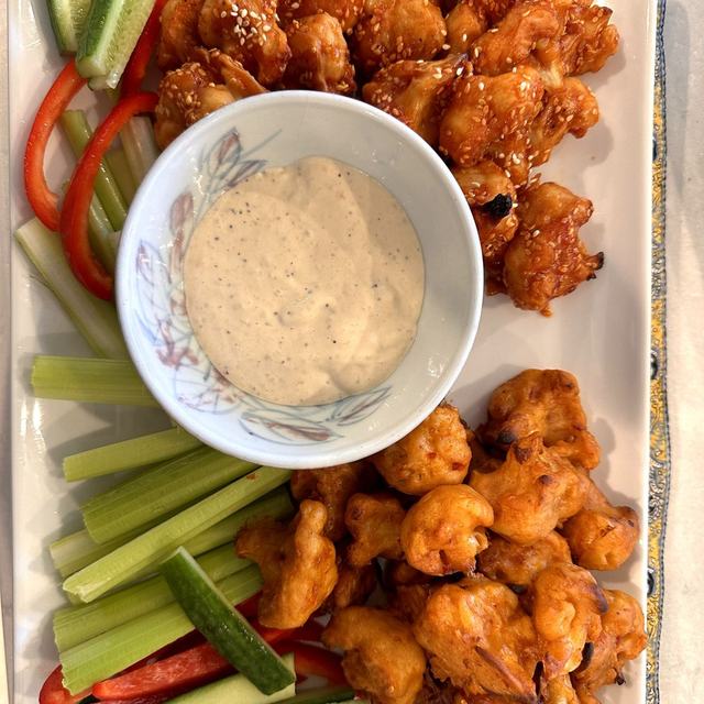 Crispy buffalo cauliflower on a platter with celery, cucumber, and red pepper sticks around a bowl of blue cheese yogurt dip