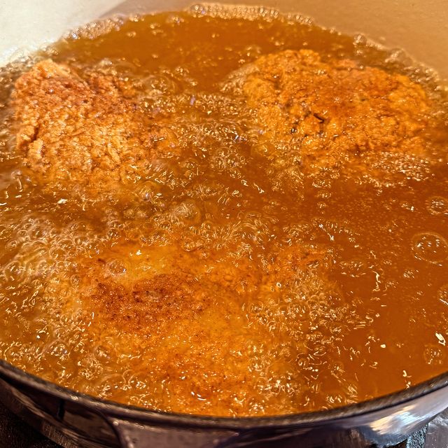 Chicken frying in bubbling oil in an enamelled Dutch oven