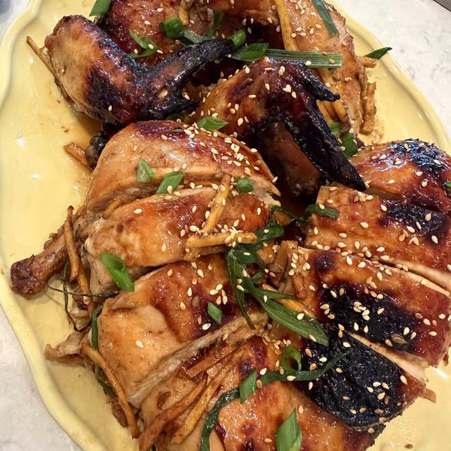 Honey soy glazed roast chicken carved on a yellow platter with sesame, ginger and green onion