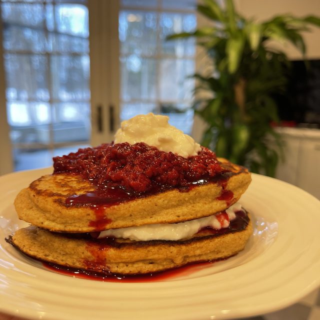 A stack of oatmeal pancakes layered with cottage cheese and topped with berry compote