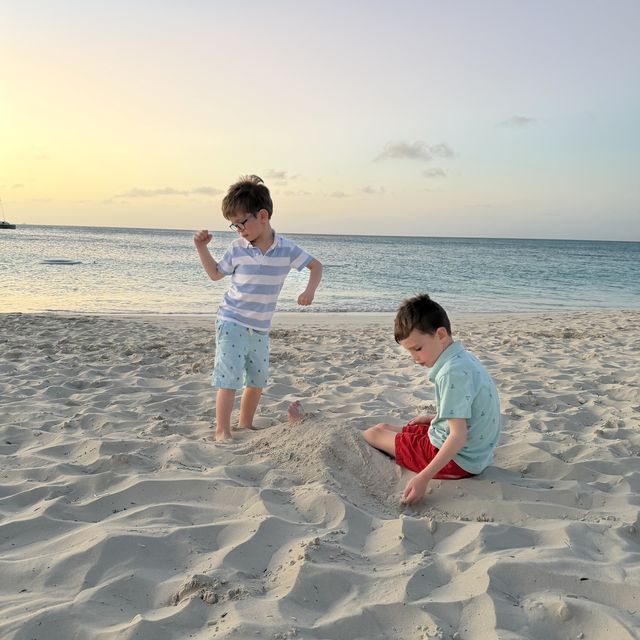 Two kids on a white sand beach in Turks and Caicos, one mid-dance, with turquoise water behind