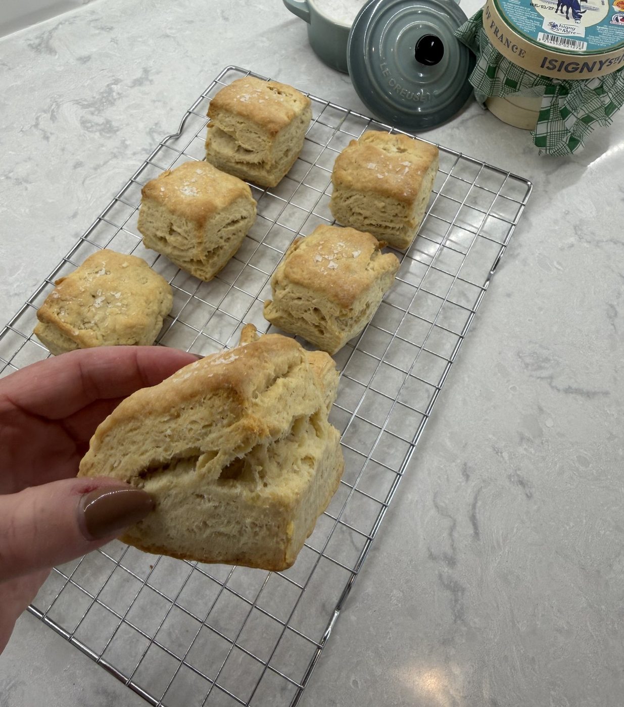 A hand pulling apart a flaky square biscuit to show its layers